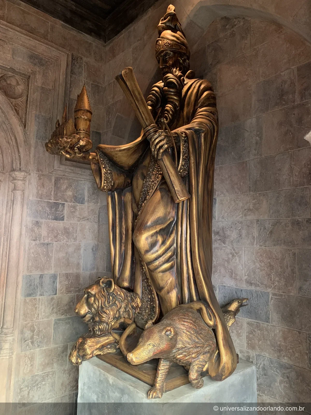 Estátua dourada de bruxo segurando uma maquete do castelo, num corredor do percurso