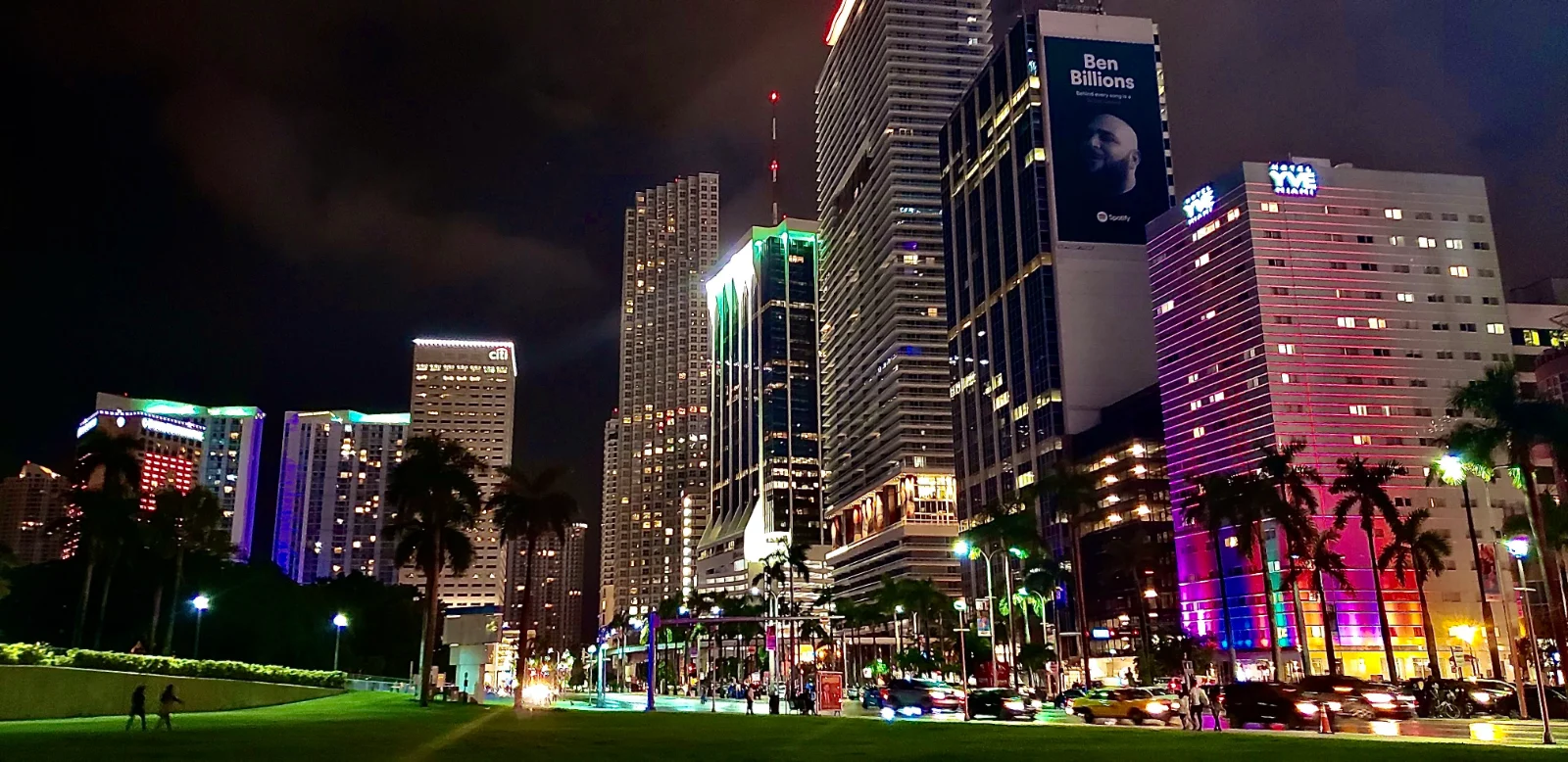 Prédios iluminados no centro de Miami à noite, vistos da avenida com palmeiras